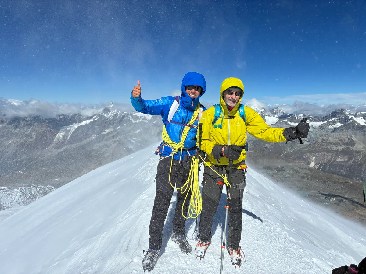 Deux alpinistes souriants, encordés au sommet d’une arête enneigée
