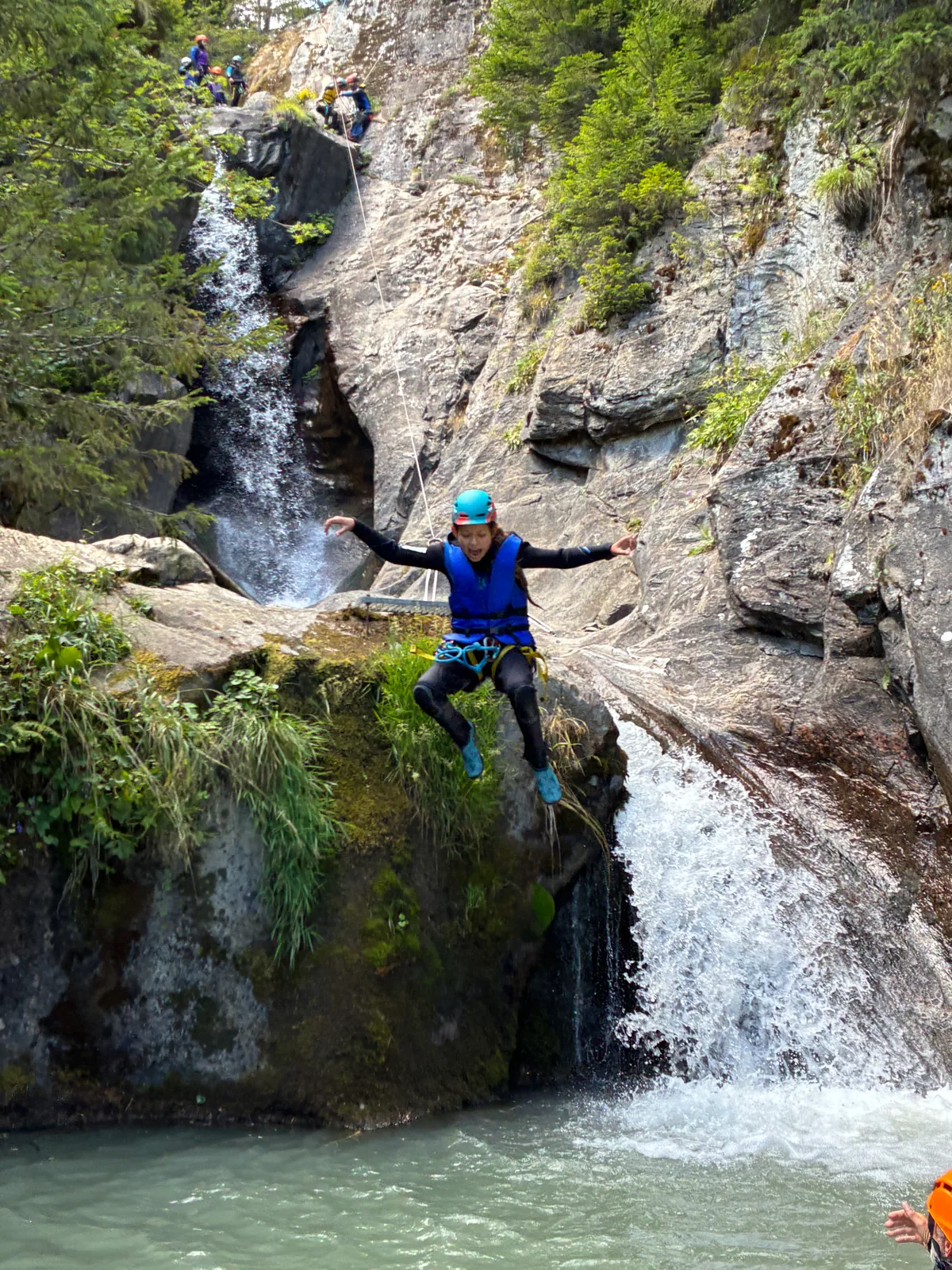Un participant casqué saute dans une vasque près d’une cascade