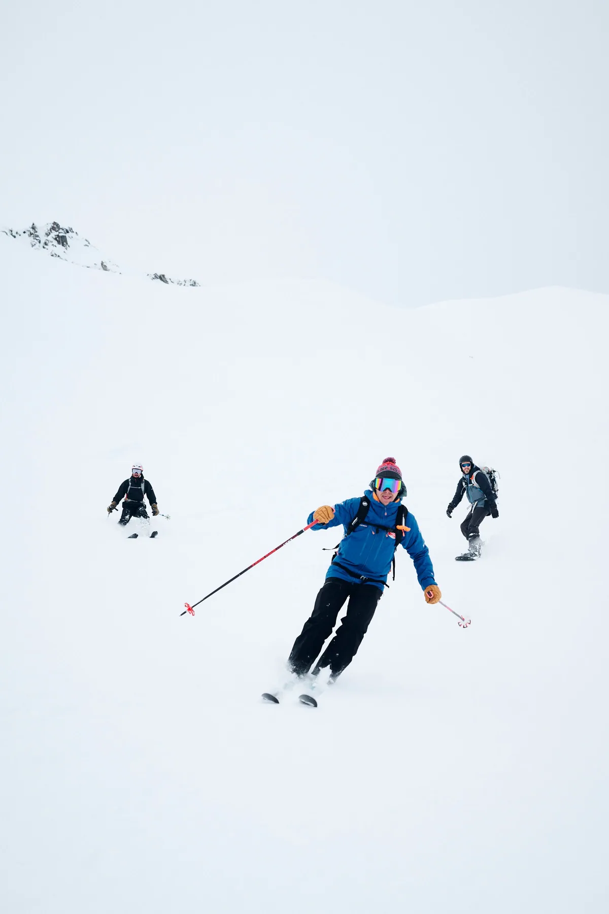 Un skieur en veste bleue descend dans la poudreuse, suivi par son groupe